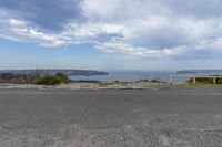 a empty road with benches at the end overlooking the ocean and lake and a blue sky