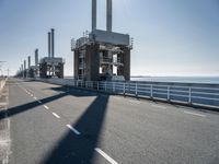 a bridge over the ocean with construction equipment in the background and two people walking on it