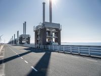 a bridge over the ocean with construction equipment in the background and two people walking on it