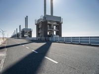 a bridge over the ocean with construction equipment in the background and two people walking on it