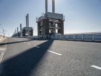 a bridge over the ocean with construction equipment in the background and two people walking on it