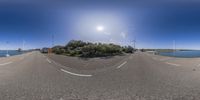 a panorama lens shot of a road along the coast with wind turbine on left side