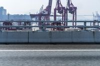 a city skyline seen from the highway of a harbor with many cranes in view and a person walking a bike