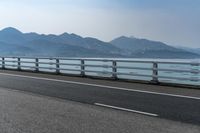 a motorcycle driving on an open highway with a view of the sea and mountains in the background