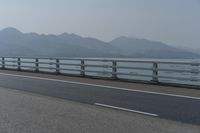 a motorcycle driving on an open highway with a view of the sea and mountains in the background