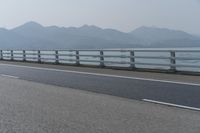 a motorcycle driving on an open highway with a view of the sea and mountains in the background