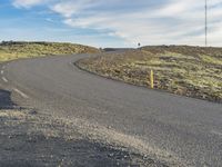 a road that has gravel next to it and some grass in the background and a lone person on a bike