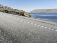 a road next to a lake with two large rocks on the sides of it and hills in the background