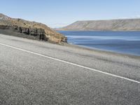 a road next to a lake with two large rocks on the sides of it and hills in the background