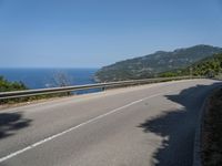 a motorcycle riding along the side of a scenic road near the ocean on a clear day