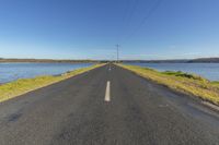 a long paved road next to a lake and a power line in the background under a blue sky