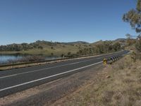 a view of a long, empty road beside the water and some hills with trees