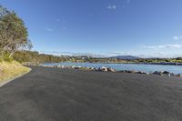 a road on a lake with stones and water in the background and a view of a blue sky