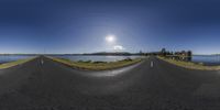 some street and a lake under the sun and a cloud filled sky that looks like some circles