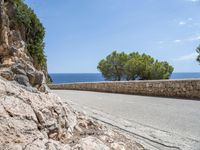 a long road on a rocky hill near water and trees with blue sky and clouds