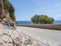 a long road on a rocky hill near water and trees with blue sky and clouds