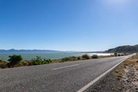 an empty road along the shore line of a large body of water with mountains in the background