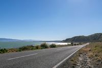 an empty road along the shore line of a large body of water with mountains in the background