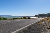 an empty road along the shore line of a large body of water with mountains in the background