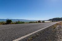 an empty road along the shore line of a large body of water with mountains in the background