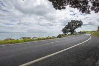 an empty asphalt road with an ocean view in the background and a sign hanging from a tree