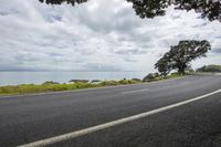 an empty asphalt road with an ocean view in the background and a sign hanging from a tree