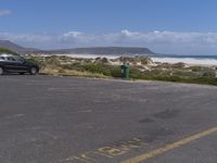 two vehicles on the road, one being parked by the beach while another is parked by the water