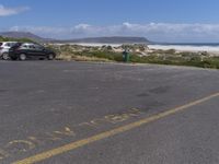 two vehicles on the road, one being parked by the beach while another is parked by the water