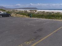 two vehicles on the road, one being parked by the beach while another is parked by the water