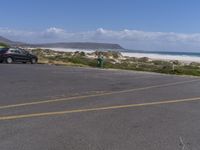 two vehicles on the road, one being parked by the beach while another is parked by the water