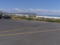 two vehicles on the road, one being parked by the beach while another is parked by the water