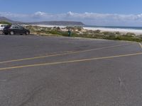 two vehicles on the road, one being parked by the beach while another is parked by the water