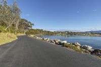 a paved road on the edge of water and land with homes along the waterline