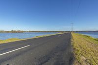 an empty road and water on the side of a lake next to power lines and poles