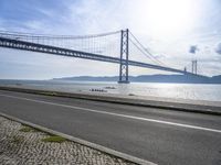 an empty road in front of the water with a bridge over it and cars driving underneath it