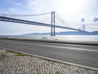 an empty road in front of the water with a bridge over it and cars driving underneath it