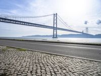 an empty road in front of the water with a bridge over it and cars driving underneath it