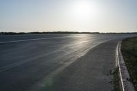 an empty road near a beach and waves as well as cars on the sand and houses on the beach