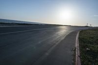 an empty road near a beach and waves as well as cars on the sand and houses on the beach