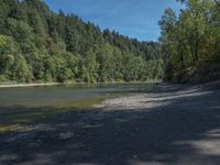 a body of water surrounded by lots of trees, near mountains and grass area with a bike parked