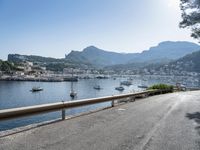 the road is going along a hillside with boats docked near it, including on to small town buildings and mountains