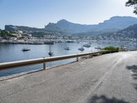 the road is going along a hillside with boats docked near it, including on to small town buildings and mountains