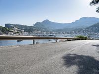 the road is going along a hillside with boats docked near it, including on to small town buildings and mountains