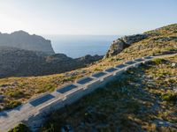 a small concrete pathway on top of a hill next to the ocean, with grass and bushes growing on the side