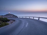 a curved road over the ocean with a beautiful sunset behind it, and the ocean in the distance