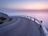 a curved road over the ocean with a beautiful sunset behind it, and the ocean in the distance