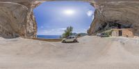 a car driving down the road in front of an entrance to a cave with a cliff