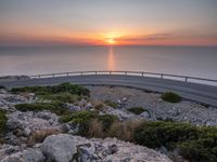 rocks along a road overlooking a large body of water at sunset time with cars driving on the track