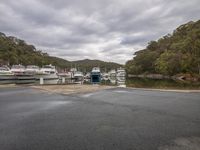 several boats docked at a marina on the side of the road under a dark, cloudy sky