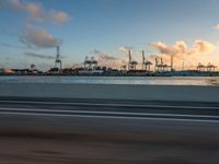 a beach with boats and cranes in the background taken from a vehicle window at dusk